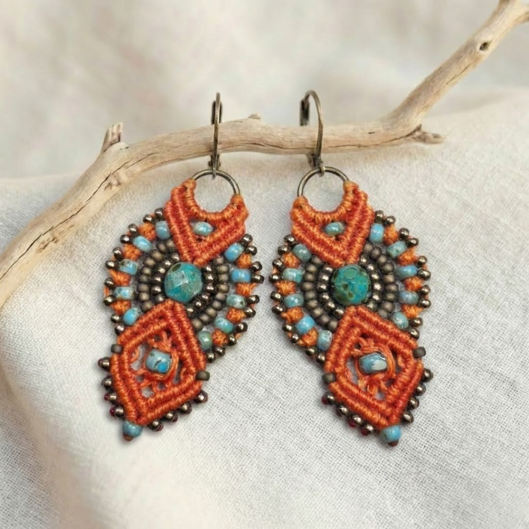 עגילי מקרמה אינקה כתום וטורקיז עם חרוזי זכוכית תלויים על ענף מעל בד פשתן