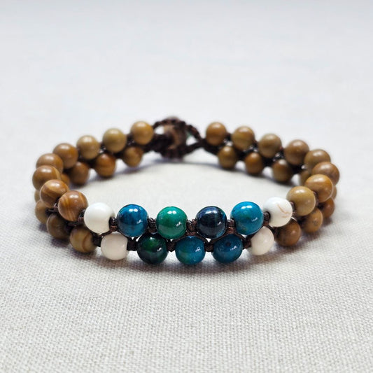 צמיד מקרמה עם אבני ג'ספר ווד גריין, קריסוקולה והיולייט מונח על בד בגוון טבעי, תקריב קשירת החוט ושילוב האבנים