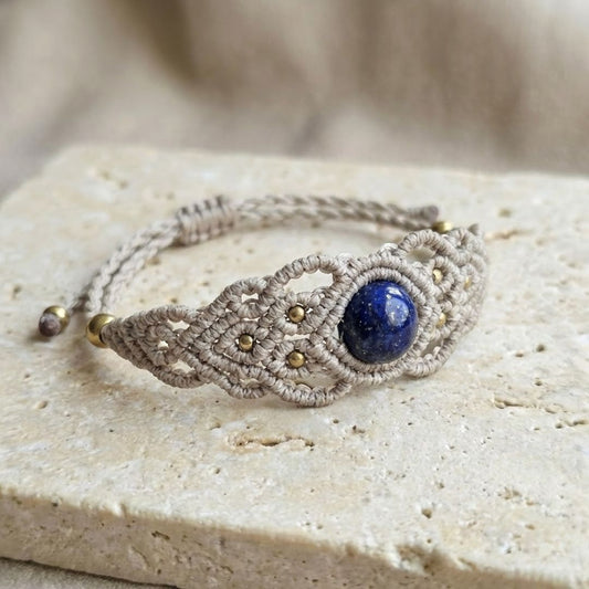 תקריב צמיד 'גאיה' בז' עם לאפיס כחול עמוק וחרוזי בראס על משטח אבן בהיר, סגירה מתכווננת קשירה ידנית