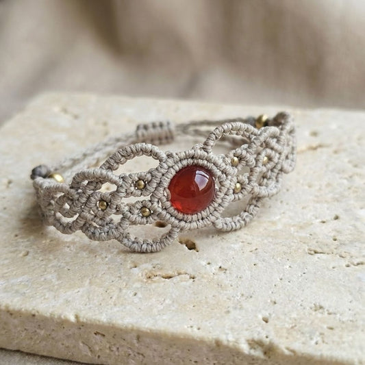 צמיד 'גאיה' בז' עם קרנליאן וחרוזי בראס על משטח אבן בהיר, דגש על סריגת חוט שעווה