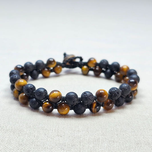 תקריב צמיד מקרמה עם אבני בזלת שחורות ואבני עין הנמר בגווני חום זהוב מונח על בד בגוון טבעי