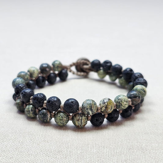 צמיד מקרמה עם אבני ג'ספר זברה ובזלת מונח על בד בגוון טבעי, תקריב סריגת החוט ושילוב האבנים