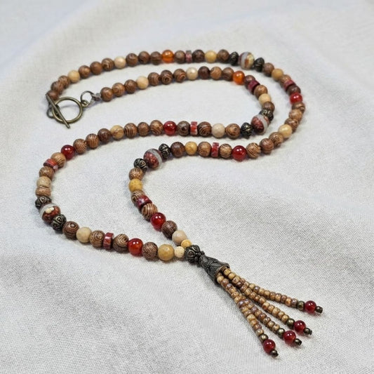 שרשרת מאלה 'אלמנט האש' מונחת על בד טבעי, מאלה אבני חן עם פיקצ'ר ג'ספר, קרנליאן וג'ספר אדום, חרוזי עץ וחרוזי פליז במראה עתיק