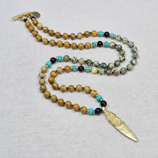 שרשרת מאלה 'קו השבט' עם אבני ווד גריין ג'ספר, פיקוק ג'ספר, חרוזי בראס ותליון שבטי מבראס על בד טבעי