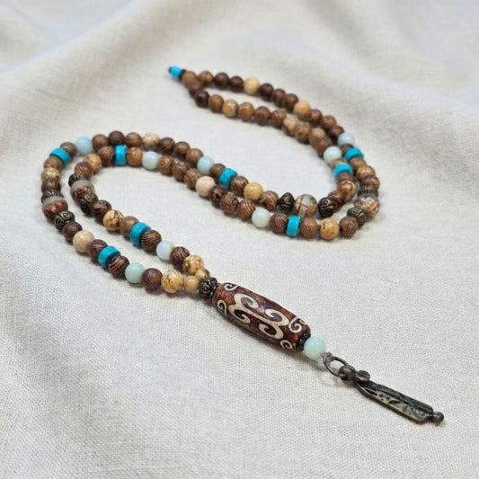 שרשרת מאלה 'אלמנט המים' מונחת על בד טבעי, מאלה אבני חן עם פיקצ'ר ג'ספר, טורקיז ואמזונייט, חרוזי עץ וחרוזי פליז עם אגת טיבטי