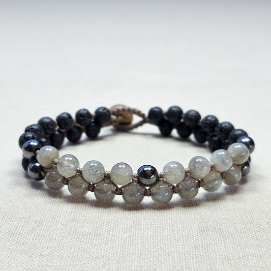 צמיד מקרמה עם אבני לברדורייט, בזלת והמטייט מונח על בד בגוון טבעי, תקריב סריגת החוט ושילוב האבנים