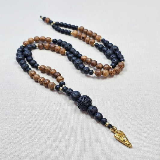 שרשרת מאלה 'רוח שבטית' מונחת על בד טבעי, מאלה אבני חן עם אבני בזלת שחורות וחרוזי עץ טבעיים ותליון חץ מבראס