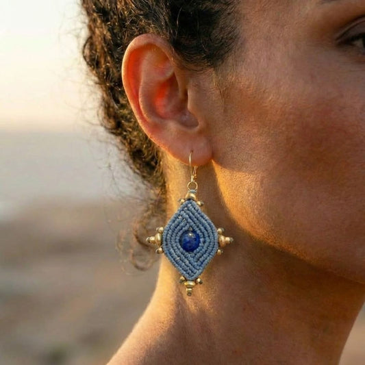 עגילי הופי כחלחל תקריב על אוזן דוגמנית, אבן לאפיס לזולי מרכזית מוקפת מקרמה וחרוזי בראס עדינים