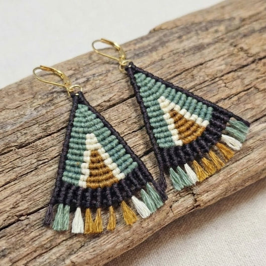 עגילי מקרמה טיפי זית וחום - זוג מלא בעבודת מקרמה עם גדילים קצרים ושוליים כהים, מונחים על ענף עץ טבעי