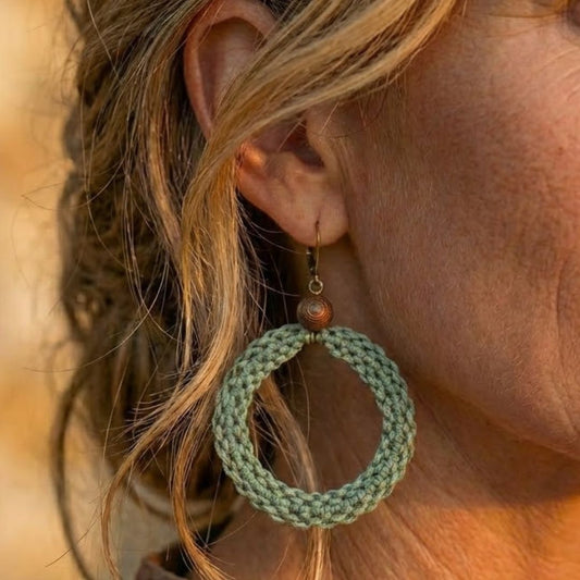 תקריב עגיל 'שיבטה' ירוק מרווה על האוזן, טקסטורת סריגת חוט שעווה מודגשת וחרוז עץ כהה