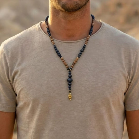 מאלה 'רוח שבטית' - מאלה לגבר עם אבני בזלת בגדלים שונים וחרוזי עץ ותליון חץ קטן מבראס, על דוגמן עם חולצה בצבע טבעי במדבר, מאלה ארוכה עד אמצע החזה