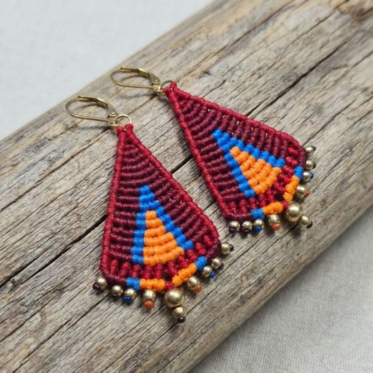 עגילי מקרמה טיפי בורדו וכתום - זוג מלא בגוונים מדורגים עם שורת חרוזי בראס, מונחים על ענף עץ טבעי