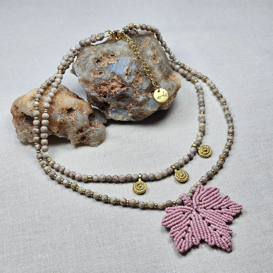 שרשרת 'אלה' ורוד עתיק מונחת על בד טבעי לצד אבנים, פוזיל קורל, תליוני בראס ותליון עלה מקרמה