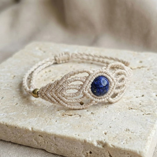 תקריב צמיד 'גאיה' בז' טבעי עם לאפיס כחול עמוק וחרוזי בראס על משטח אבן בהיר, סגירה מתכווננת קשירה ידנית