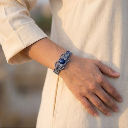 צמיד 'גאיה' כחלחל עם אבן לאפיס לזולי וחרוזי בראס על יד אישה, בשילוב גלביה בצבע שמנת באור טבעי