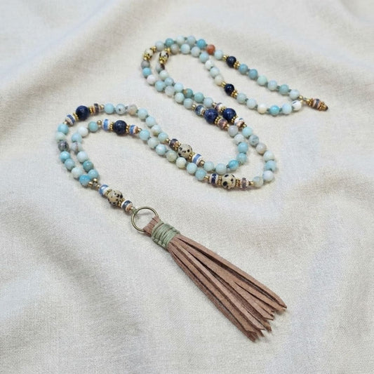 שרשרת מאלה אבני חן בעבודת יד עם אמזונייט, לאפיס לזולי וג'ספר דלמטי, חרוזי בראס וגדיל דמוי זמש, מאלה ארוכה מונחת על בד טבעי