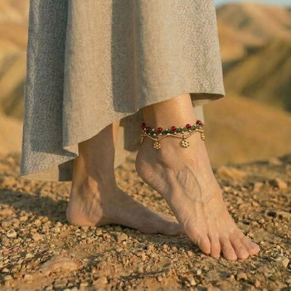 צמיד רגל פושקר ירוק עם חרוזי זכוכית אדומים ותליוני בראס על קרסול יחף במדבר