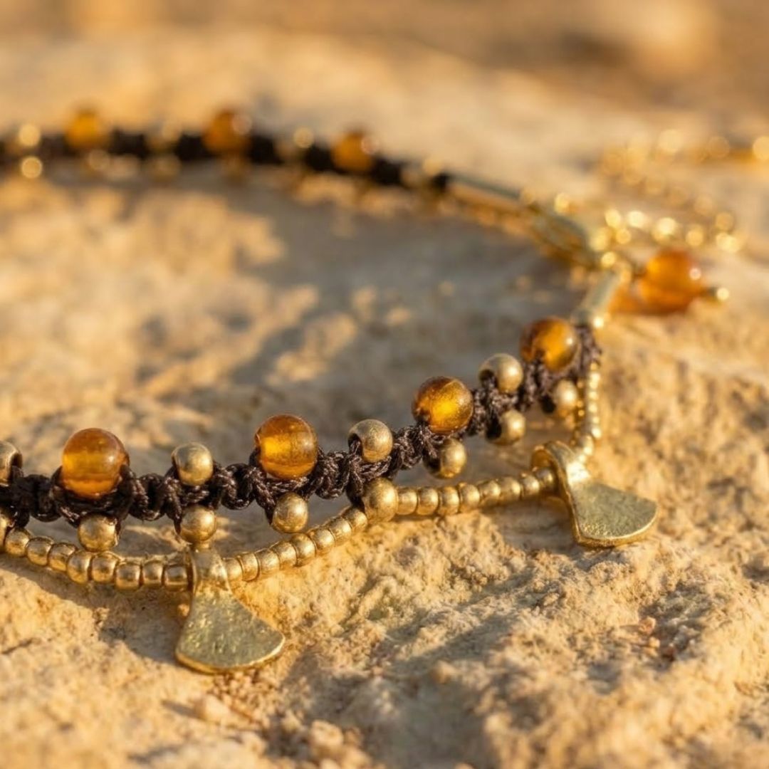 תקריב צמיד רגל פושקר חום עם חרוזי זכוכית קטנים ענבריים חרוזי בראס ותליוני מטבע עדינים