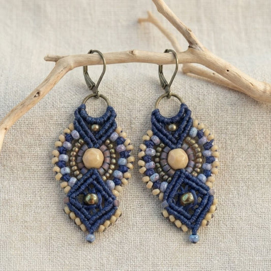 עגילי מקרמה אינקה כחול ובז' עם חרוזי זכוכית תלויים על ענף מעל בד פשתן