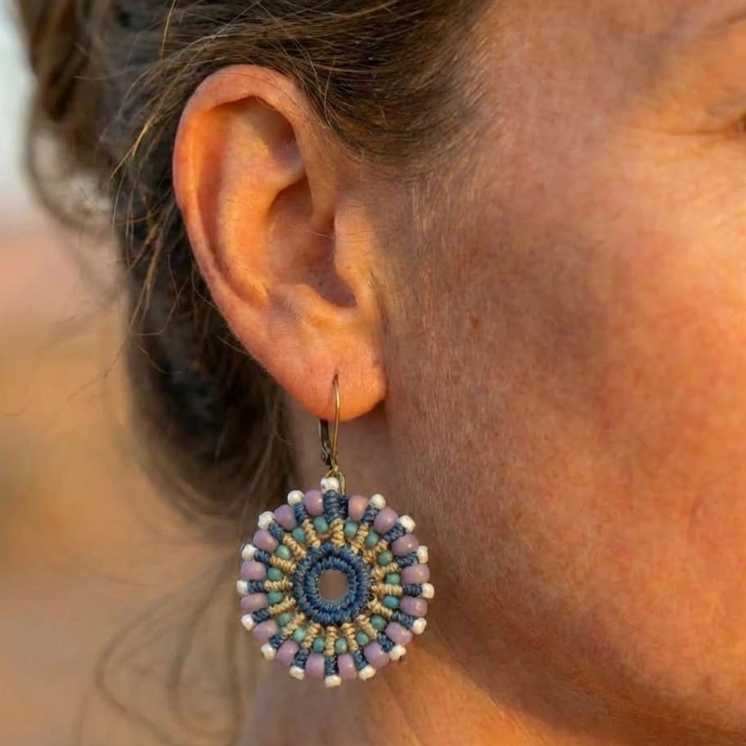 עגילי מקרמה מנדלה כחול וסגול עם חרוזי זכוכית על דוגמנית בצילום קלוזאפ ברקע מדברי