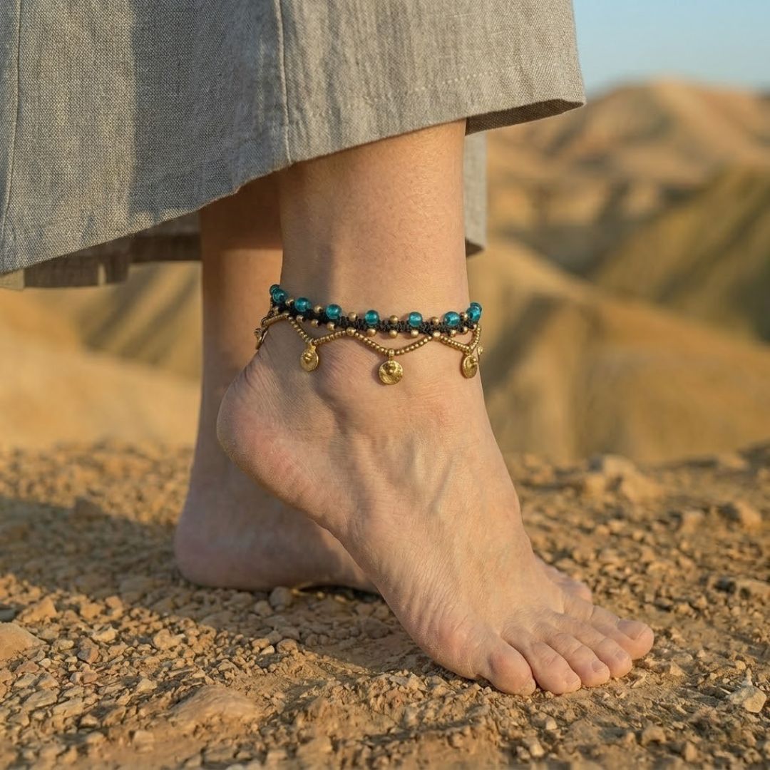 צמיד רגל פושקר שחור עם חרוזי זכוכית כחולים ותליוני מטבע מבראס על קרסול יחף במדבר
