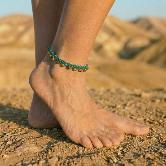 צמיד רגל מקרמה 'גואה' טורקיז עם חרוזי זכוכית ענבריים וחרוזי בראס על קרסול דוגמנית ברקע מדבר